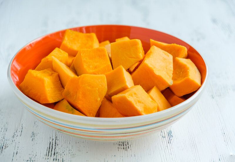 on a white wooden surface is a white and orange bowl full of cubed pumpkin