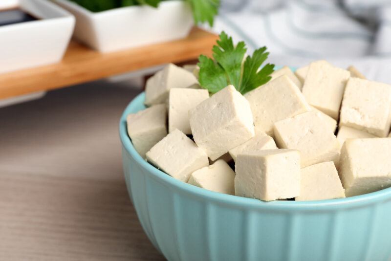 closeup image of a pale blue bowl full of cubed tofu with a sprig of cilantro on top