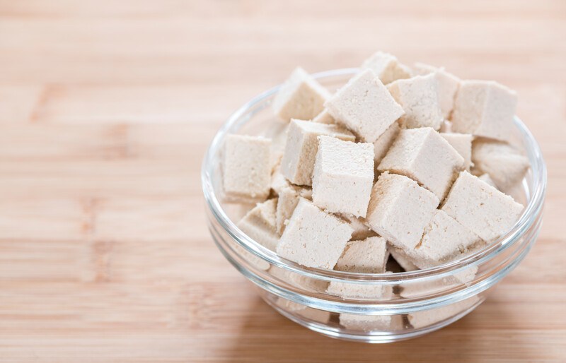 on a wooden surface is a glass clear bowl full of cubed tofu