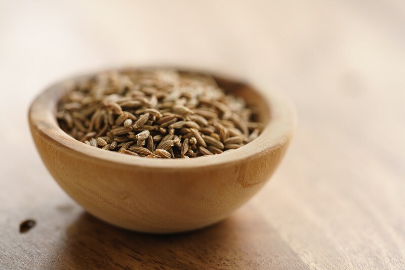 closeup image of wooden bowl full of cumin seeds on a wooden surface