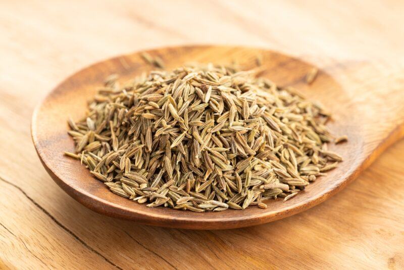 on a wooden surface is a closeup image of a wooden spoon with cumin seeds