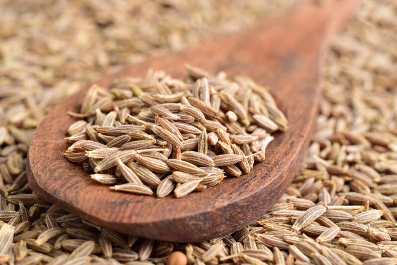 a closeup image of a spread of cumin seeds with a wooden ladle on top with cumin seeds as well