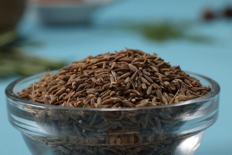 a closeup image of a clear glass bowl full of cumin seeds