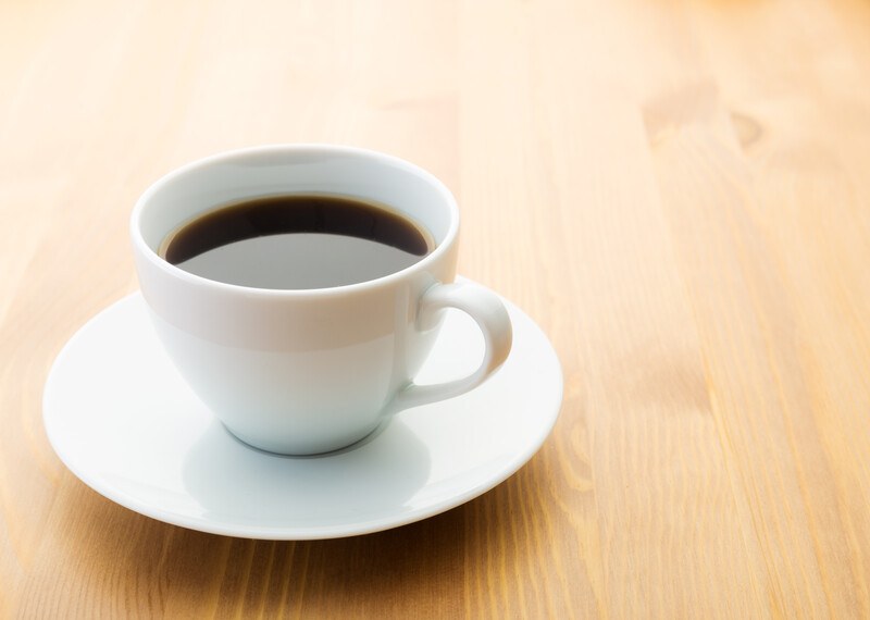 on a brown wooden surface is a white cup and saucer with black coffee in it