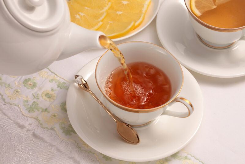 on an embroidered table cloth is a couple of cup and saucers with fresh tea, behind is a small dish with lemon slices