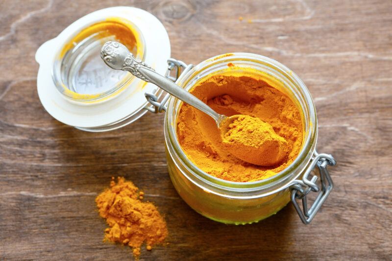 overhead shot of a mason jar with curry powder with a silver spoon beside it is a small mound of curry powder