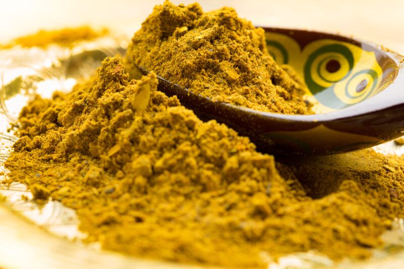 closeup image of a mound of curry powder on a plate with a printed wooden spoon