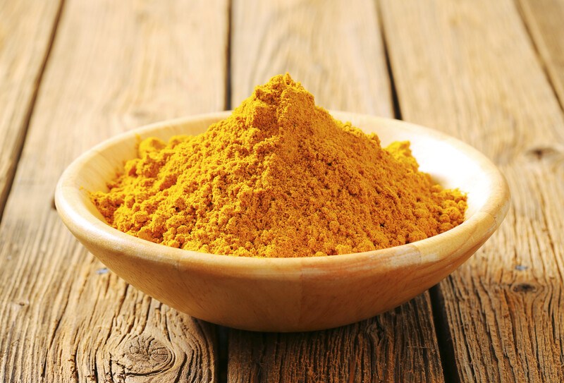 on a wooden surface is a brown wooden bowl full of curry powder