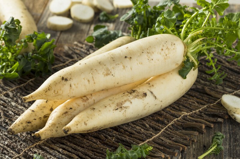 a closeup image of a pile of daikon on a dark-colored native placemat, with sliced daikon at the back