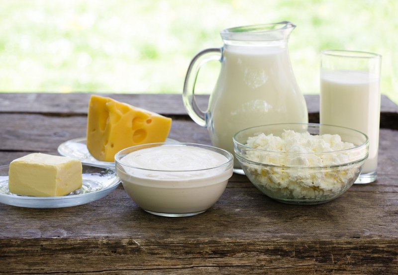 Several dairy products rest on a rustic wooden tabletop against a blurry outdoor background.