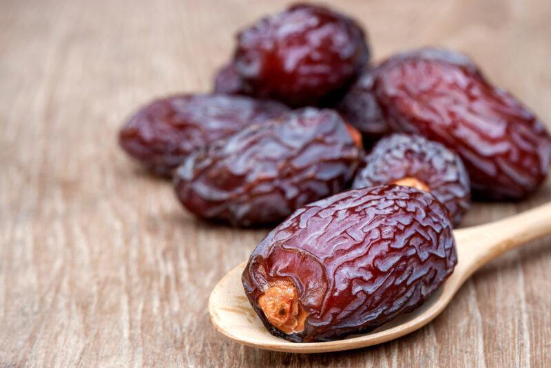 on a wooden surface is a closeup image of dried dates, one resting on a wooden spoon