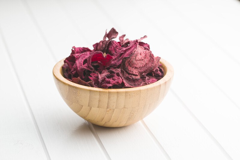 on a white wooden surface is a brown wooden bowl full of dehydrated beets