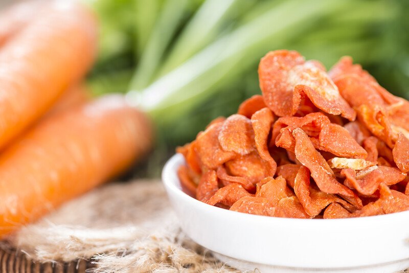 closeup image of a white dish full of dehydrated carrots with fresh carrots at the back