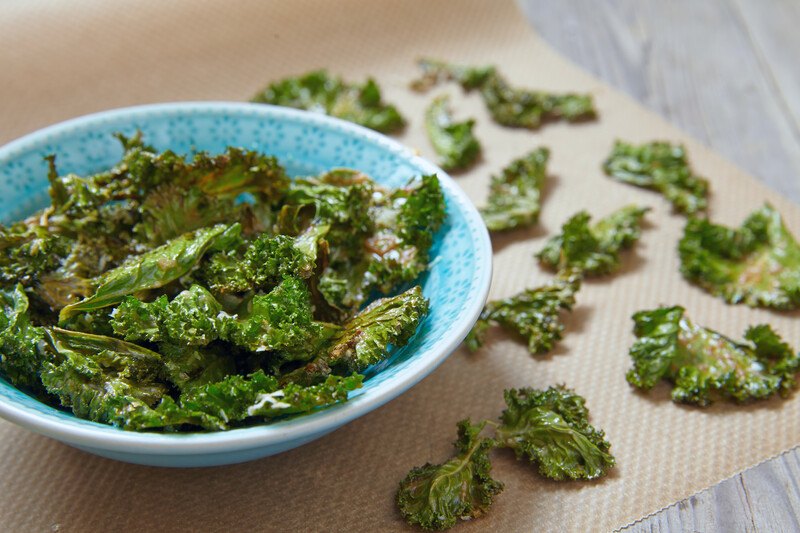 blue bowl with dehydrated kale resting on a silicone baking sheet with dehydrated kale laid out