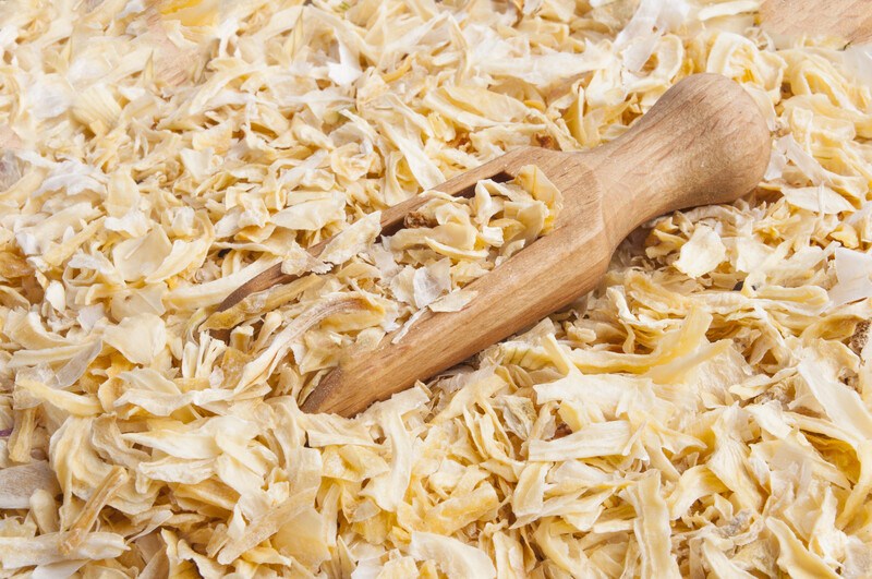 closeup shot of a pile of dehydrated onions with a wooden scoop shoved in it