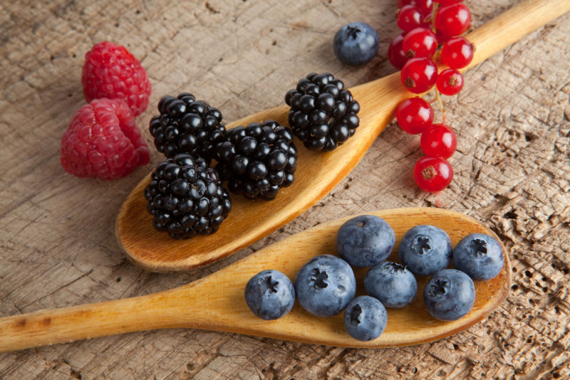 diffrent varieties of berries on two wooden spoons | Food For Net blackberries and blueberries on two wooden spoons,a few raspberries scattered on the background