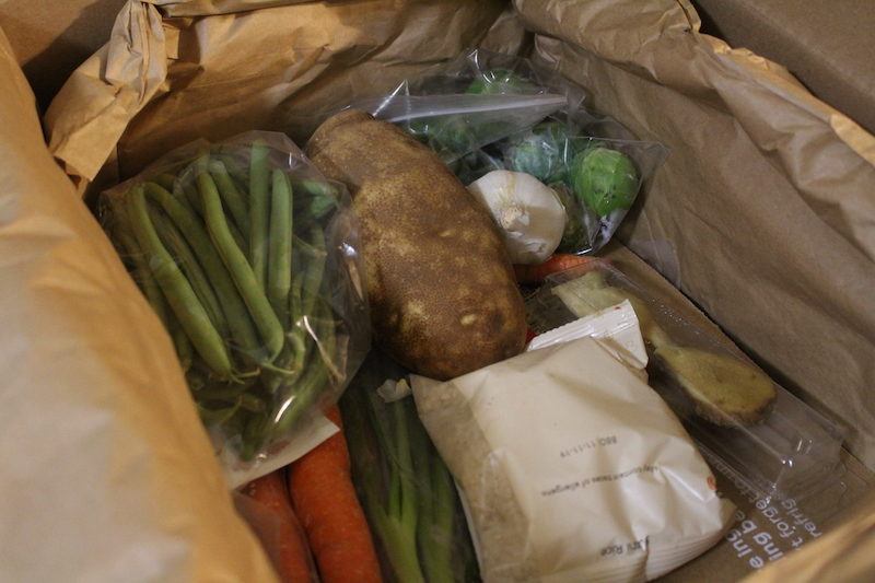 cardboard box opened with fresh vegetables inside like potatoes, carrots, and a bag of rice.