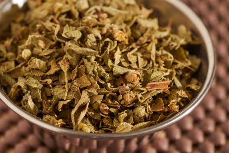 a closeup image of a brown place mat with a metal bowl full of dried Mexico oregano on it