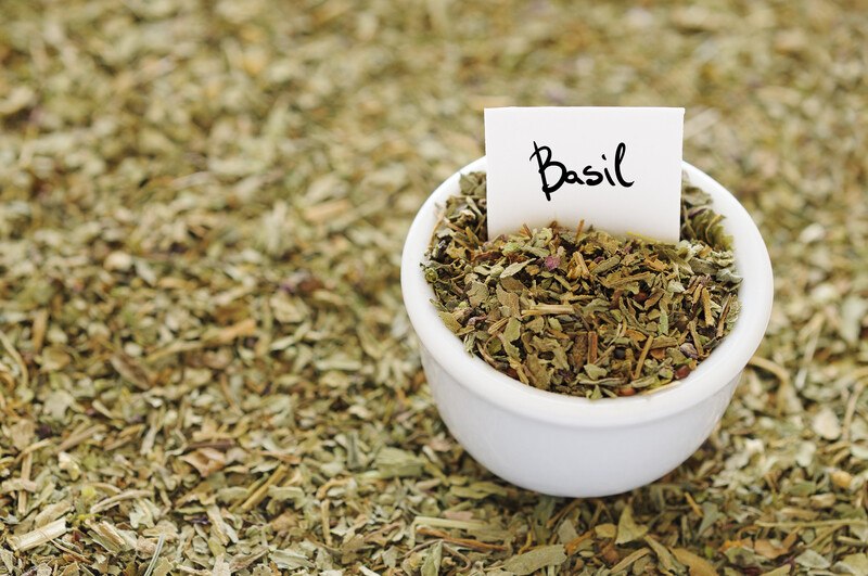 on top of dried basil is a small white bowl full of dried basil with a white paper with the word basil written on it