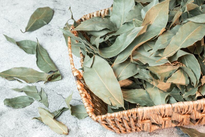 on a marble surface is a square basket with dried bay leaves, beside it are loose dried leaves