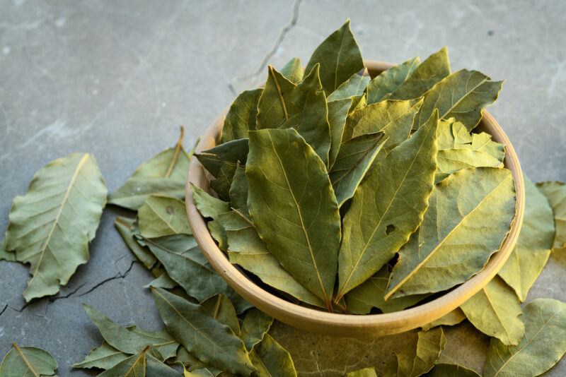 on a concrete surface is a clay bowl of dried leaves with loose dried bay leaves around it