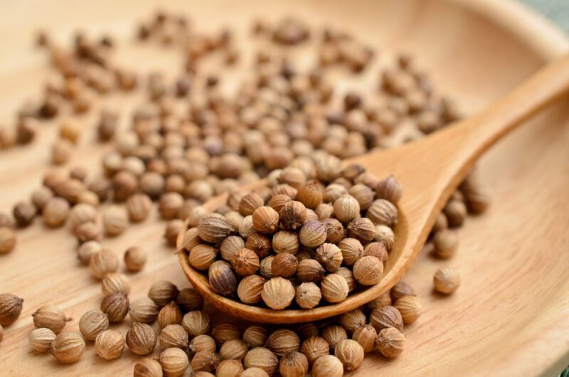 a wooden plate with dried coriander seeds with wooden spoon with dried coriander seeds as well