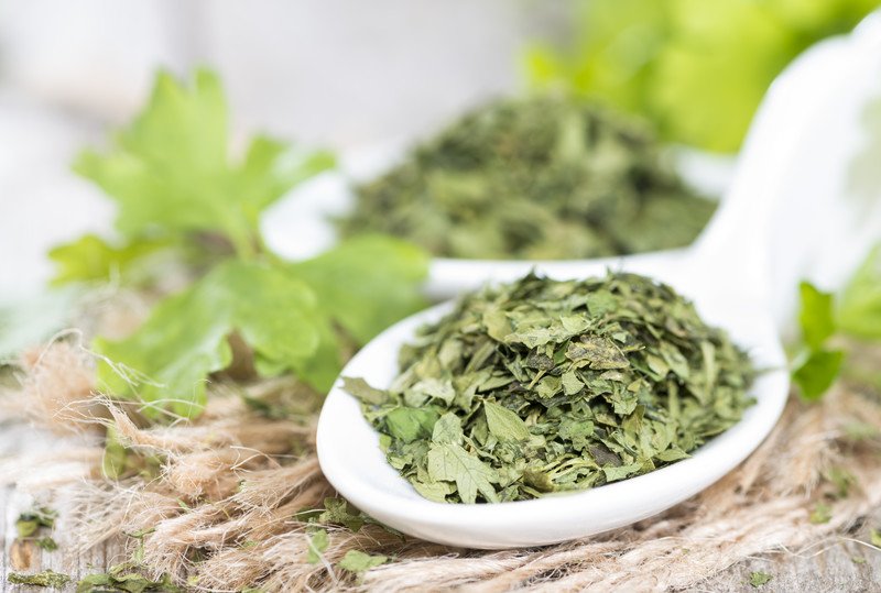 a ceramic ladle full of dried parsley with fresh parsley leaves at the back