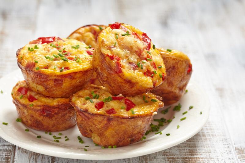 on a rustic looking white wooden surface is a white plate with a pile of egg muffins with sausage and peppers, with a liberal sprinkling of minced herbs