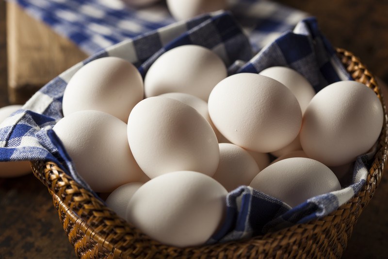 Several white eggs rest on a blue and white cloth inside a brown wicker basket.