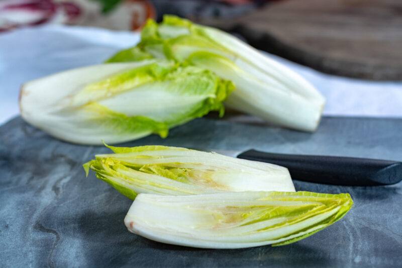 on a blue marble chopping board are quartered endives with a knife with black handle beside it