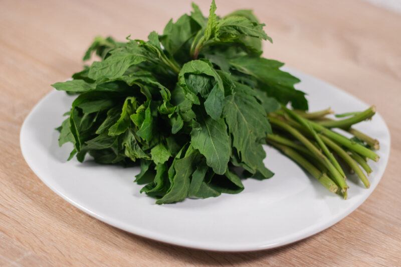 on a wooden surface is a white square dish with a bunch of fresh epazote on it