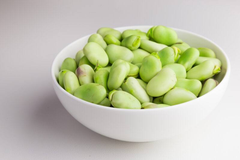 on a white surface is a white bowl full of fava beans