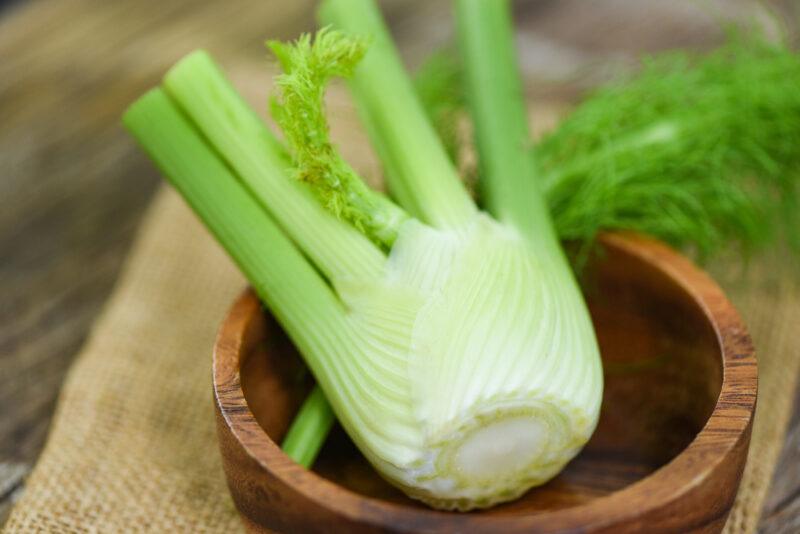 on a wooden surface is a wooden bowl with a fennel, resting on top of burlap table mat