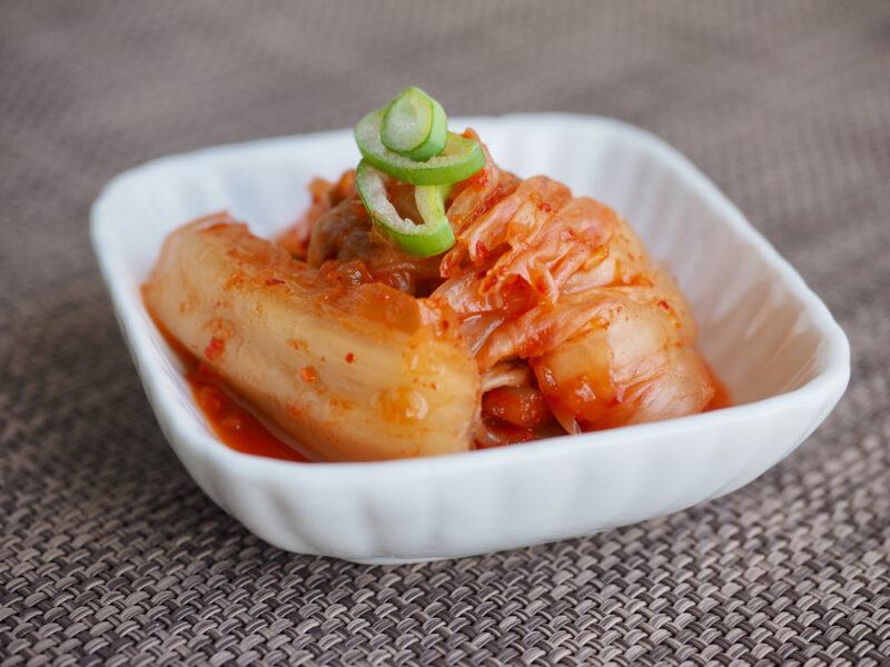 closeup image of a small square ceramic dish with fermented napa cabbage, kimchi, with thinly sliced celery on top