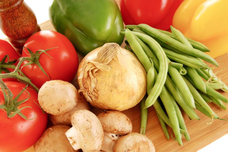 bell peppers, tomatoes, onions, green beans and mushrooms on a chopping board.