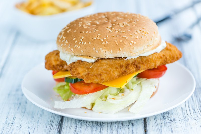 a fish sandwich on a plate on a wooden table to represent chick fil a's fish sandwich  