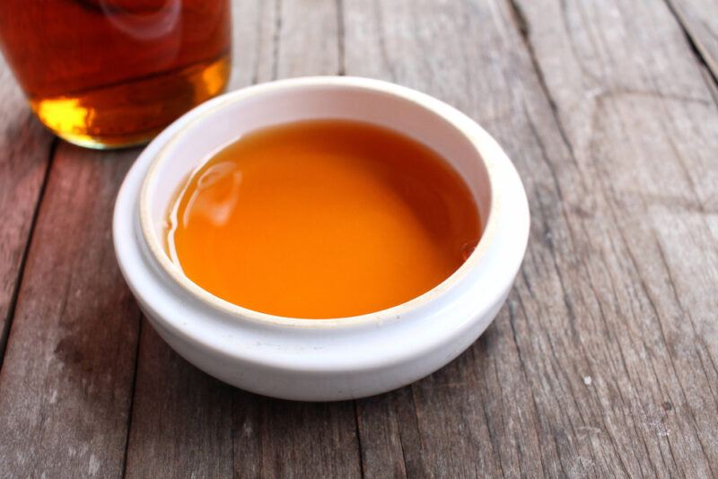 on an aged wooden surface is a white dish with fish sauce, behind it is partial image of a bottle of fish sauce