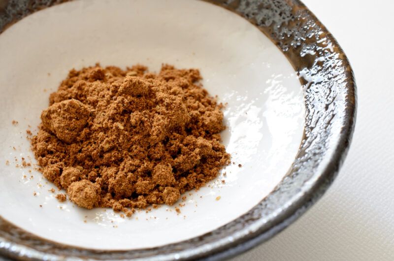 a closeup image of a white ceramic bowl with dark brown rim with a small mound of five-spice