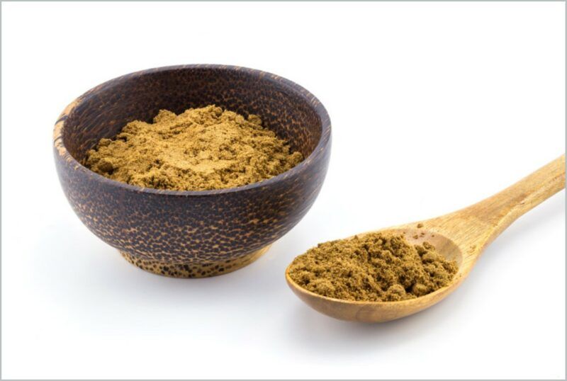 a dark brown wooden bowl and light brown wooden ladle full of five-spice against a white background