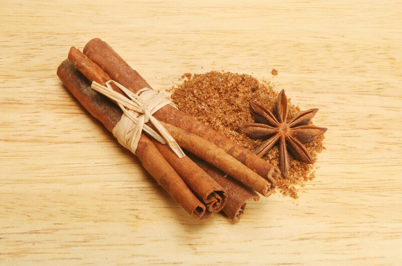 on a light-colored wooden surface is a bundle of cinnamon sticks, star anise, and a mound of five-spice