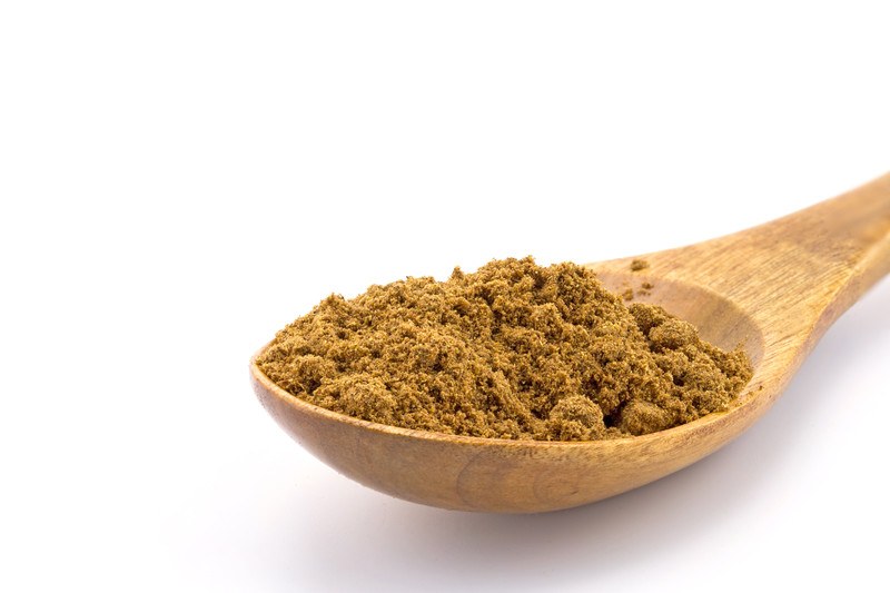 closeup image of a wooden ladle full of five-spice against a white background