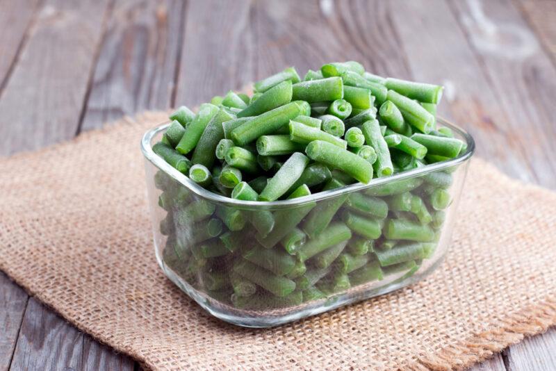 on a rustic wooden surface is a small rectangular container full of frozen green beans, resting on top of a piece of burlap