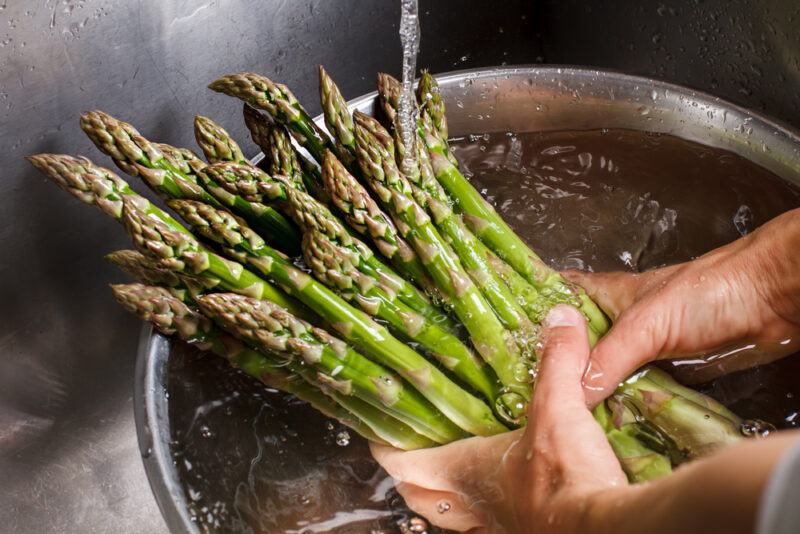 man's hand holding a bunch of fresh asparagus in a basin full of water under a running water