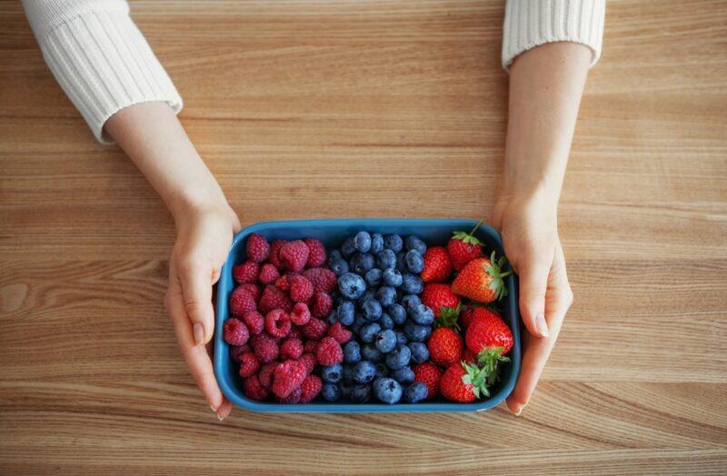 overhead shot of a couple of hands holding out a small tray of fresh different berries like raspberries, blueberries, and strawberries