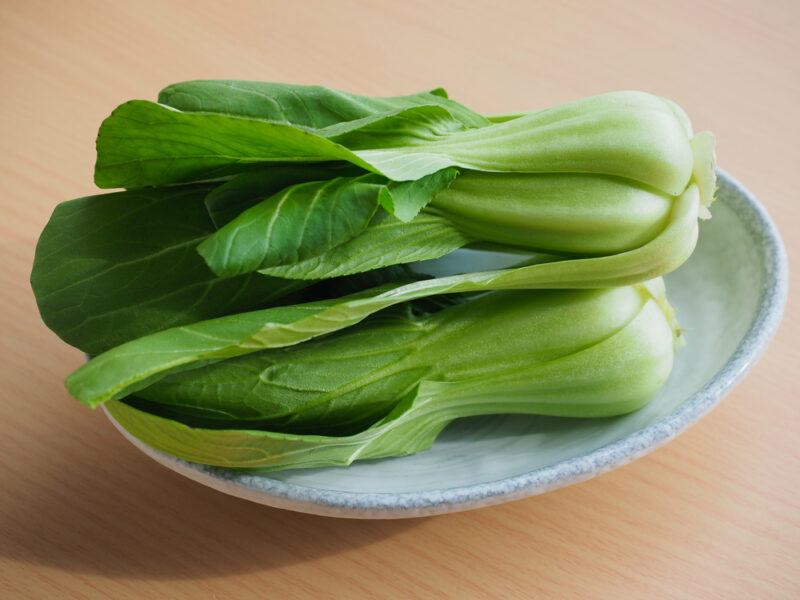 on a wooden surface is a dish with a pile of fresh bok choy