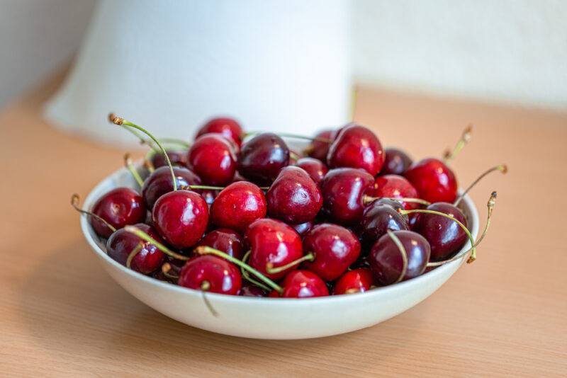 on a wooden surface is a small white dish of fresh cherries