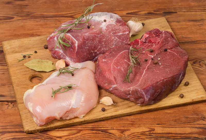 on a wooden surface is a chopping board with fresh chicken breast, pork, beef on it, sprinkled with herbs and spices