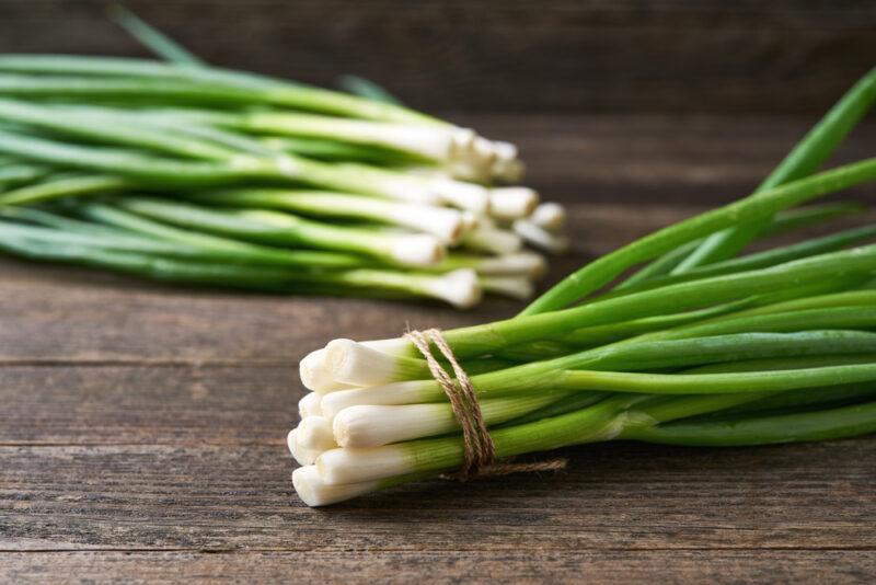 on an aged wooden surface is a couple of bunches of fresh chives