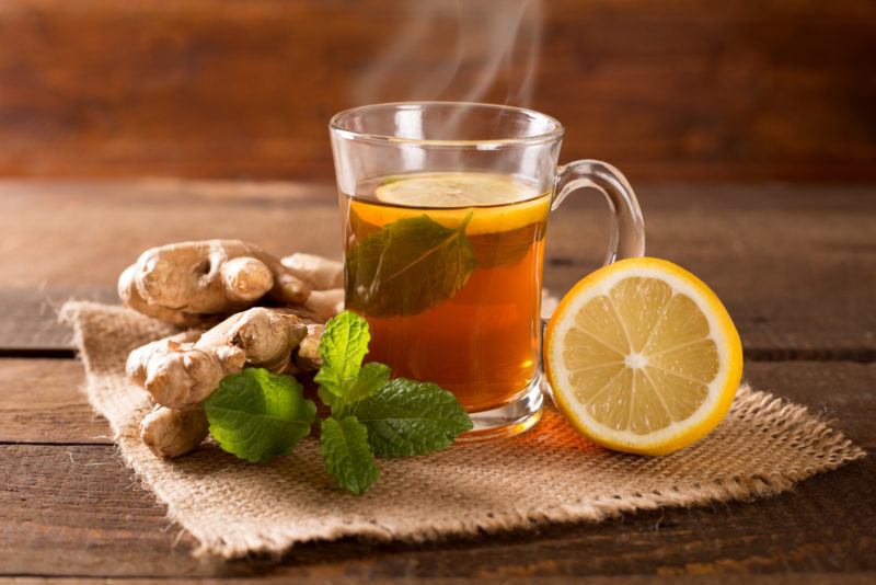 a glass of ginger tea, fresh ginger and half a lemon on a woven placemat.