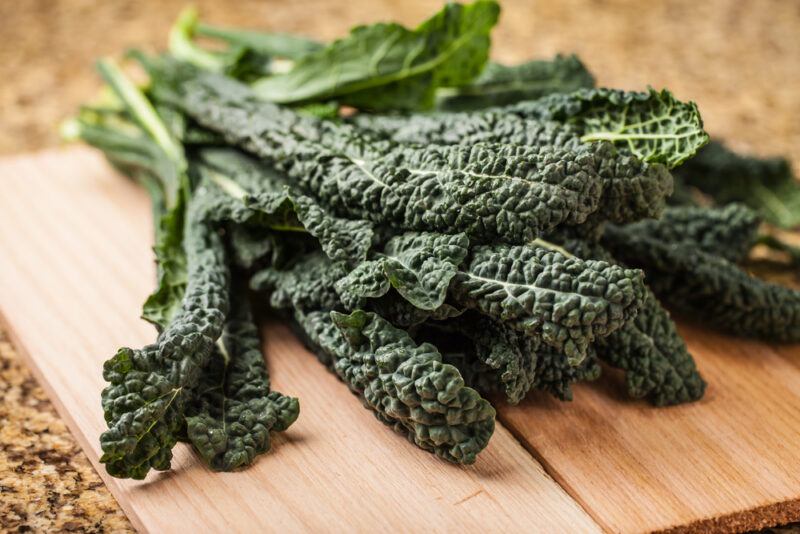 on a wooden chopping board is a bunch of fresh kale, a dark leafy green vegetable